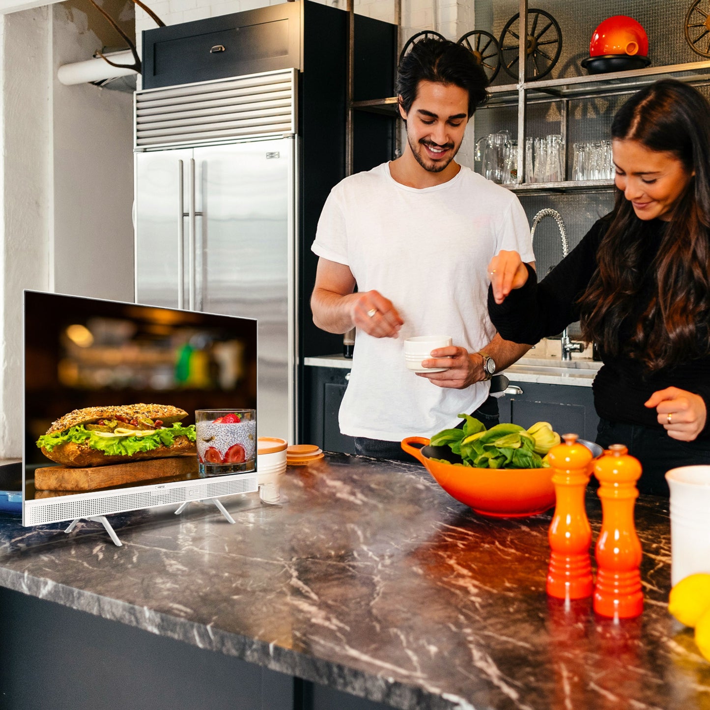 METZ Bærbar 12 V Google TV 32" viser sandwich og drik på skærm, omgivet af grøntsager, skål og orange kværne.