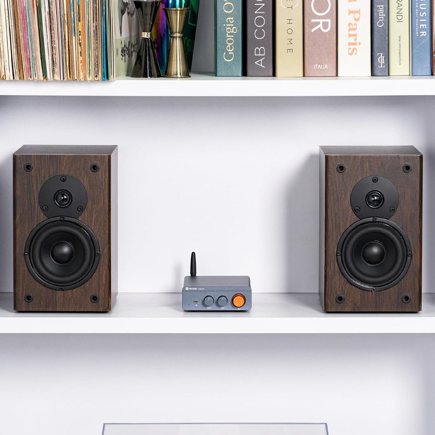 Fosi Audio forstærker Bluetooth 2x100W, stor orange knap, sammen med træsatelithøjttalere på hylde.