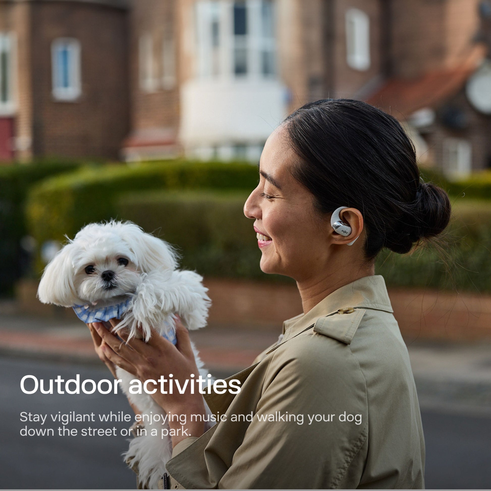 Shokz OpenFit 2+ TWS øretelefoner grå bæres af kvinde udendørs, lille hund i armene, tekst: Udendørs aktiviteter.