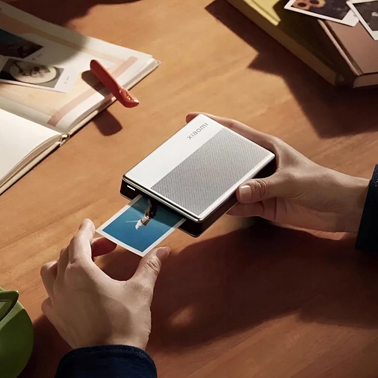 Xiaomi Bærbar fotoprinter 1S kompakt ZINK Zero Ink printer printblå billede, vises i hånd med foto, på træbord.