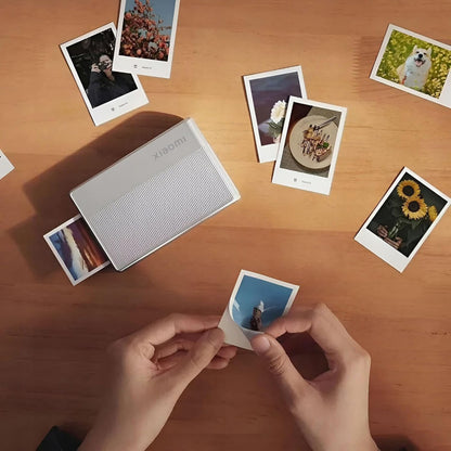 Xiaomi Bærbar fotoprinter 1S ZINK Zero Ink, printer på træbord med udskrift og fotos af blomster, mad og hund.