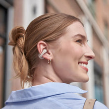 Shokz OpenDots One grå trådløse åbne clip-on-hovedtelefoner båret af kvinde med blond knold og guld øreringe.