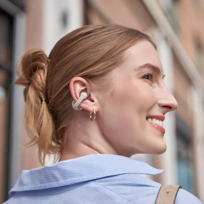 Shokz OpenDots One grå trådløse åbne clip-on-hovedtelefoner båret af kvinde med blond knold og guld øreringe.
