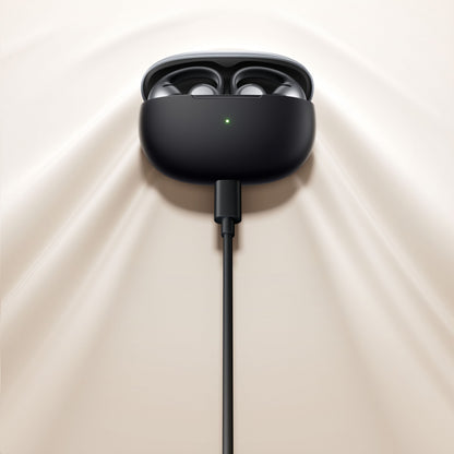 Shokz OpenDots One trådløse åbne clip-on høretelefoner i åbent opladningsetui med grøn LED, cremefarvet underlag.