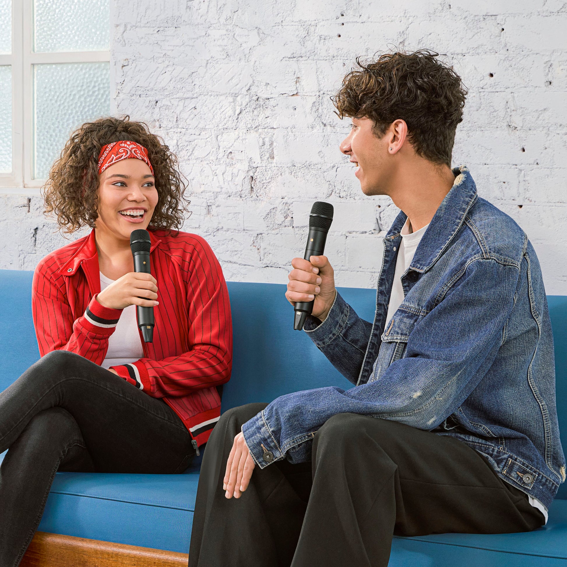 Røde Interview trådløs mikrofon med GainAssist holdes af kvinde i rød jakke og mand i denim på blå sofa.