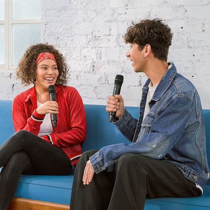 Røde Interview trådløs mikrofon med GainAssist holdes af kvinde i rød jakke og mand i denim på blå sofa.