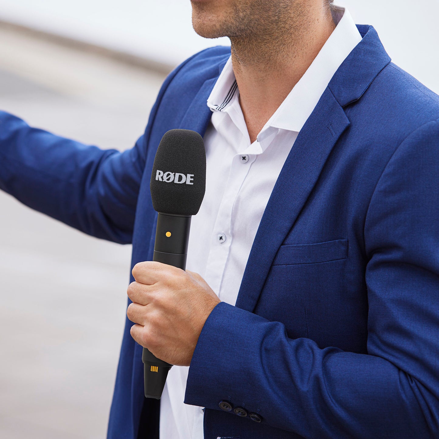 Røde Interview sorterer trådløs mikrofon med GainAssist og gul indikator, holdt af person iført blå habitus.