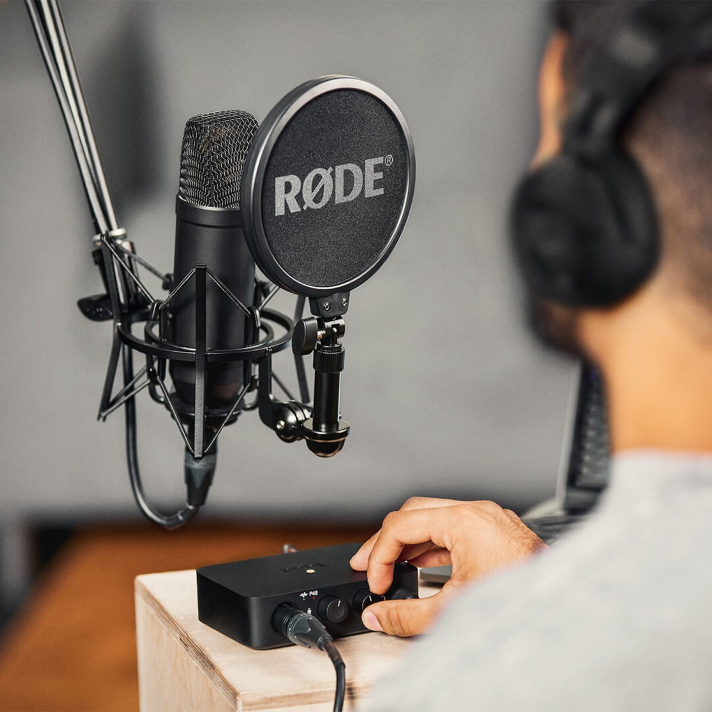 Røde NT1 + AI1 Studio Bundle med boomarm, popfilter og shock mount foran person med hovedtelefoner ved lydinterface.