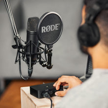 Røde NT1 + AI1 Studio Bundle med boomarm, popfilter og shock mount foran person med hovedtelefoner ved lydinterface.