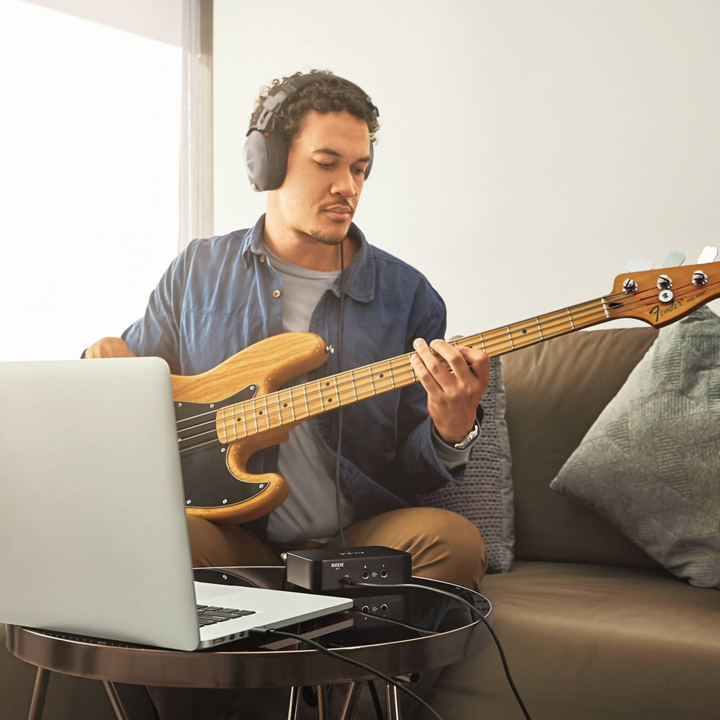 Røde NT1 + AI1 Studio Bundle mikrofon og audio interface ved laptop, el-bas og hovedtelefoner på bord i hjemmemiljø.