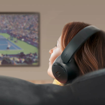 MIXX StreamQ Surround TV trådløse hovedtelefoner bæres af person i sofa foran vægmonteret tv-skærm med tenniskamp.
