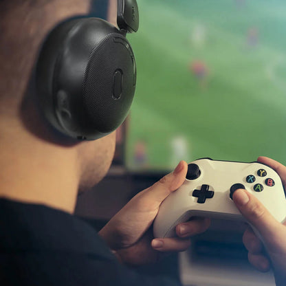 MIXX StreamQ Surround TV trådløse hovedtelefoner bæres af person med game controller, sløret sport på skærm i baggrund.