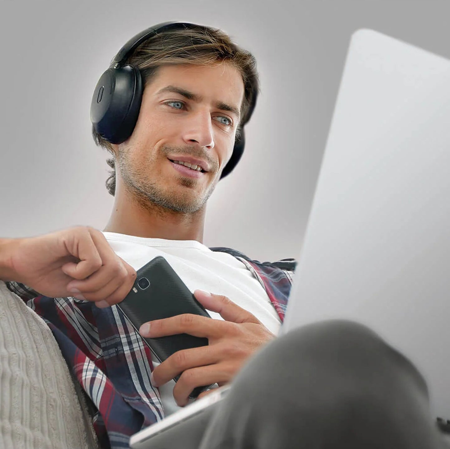 MIXX StreamQ Surround TV trådløse hovedtelefoner på mand med ternet skjorte, laptop og smartphone i hånden.