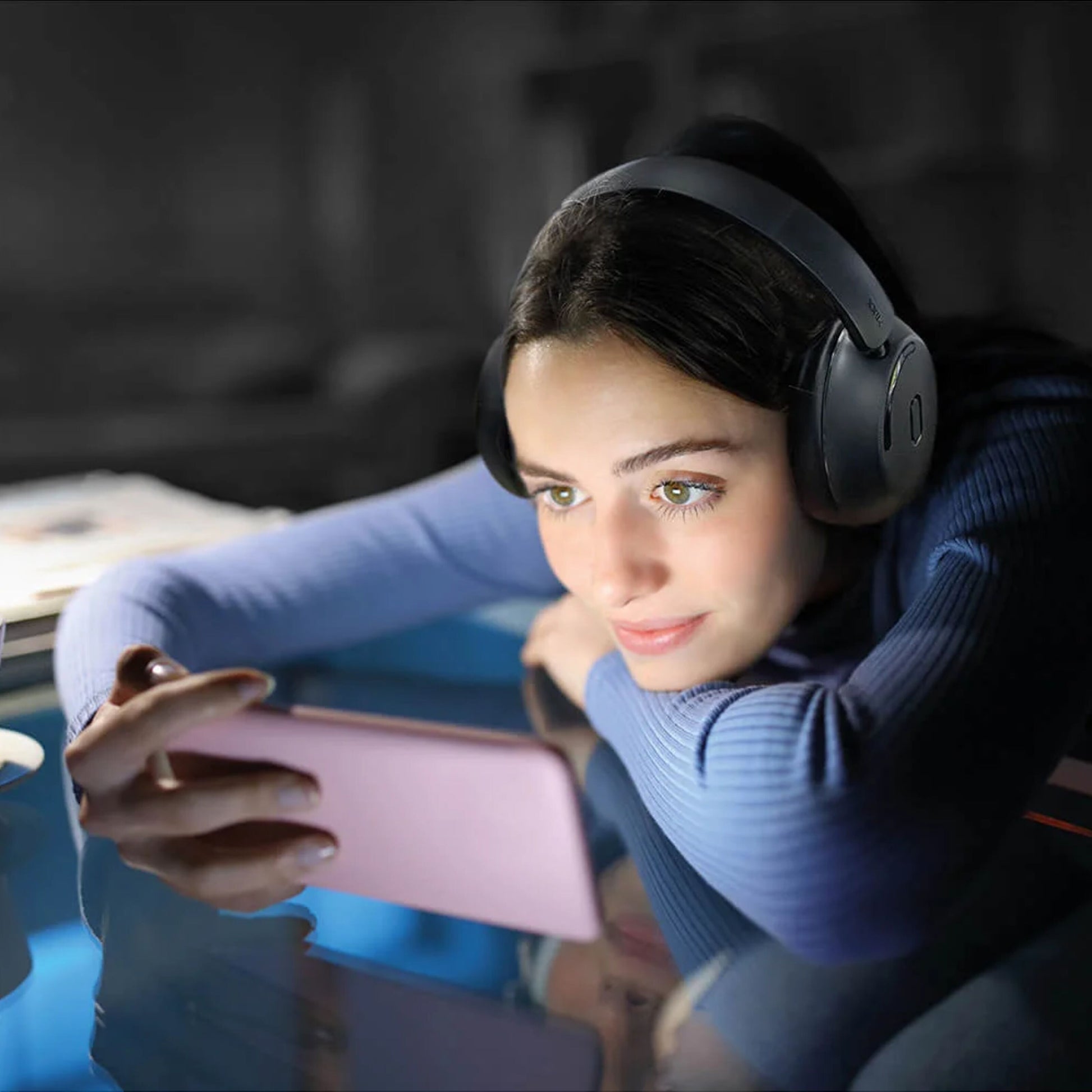 MIXX StreamQ Surround TV Trådløse hovedtelefoner på kvinde med langt mørkt hår, blå sweater, pink smartphone.