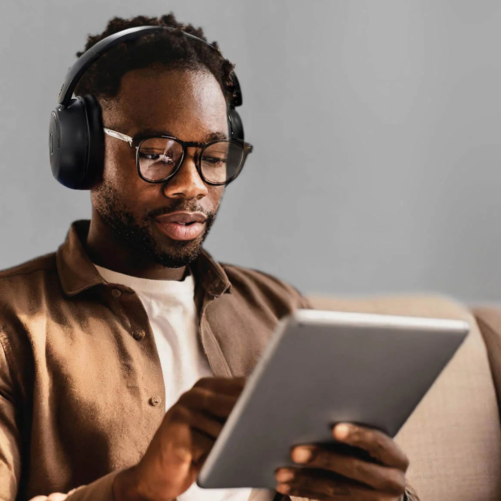 MIXX StreamQ Surround TV trådløse hovedtelefoner bæres af mand med briller, brun skjorte og hvid t-shirt på beige sofa.