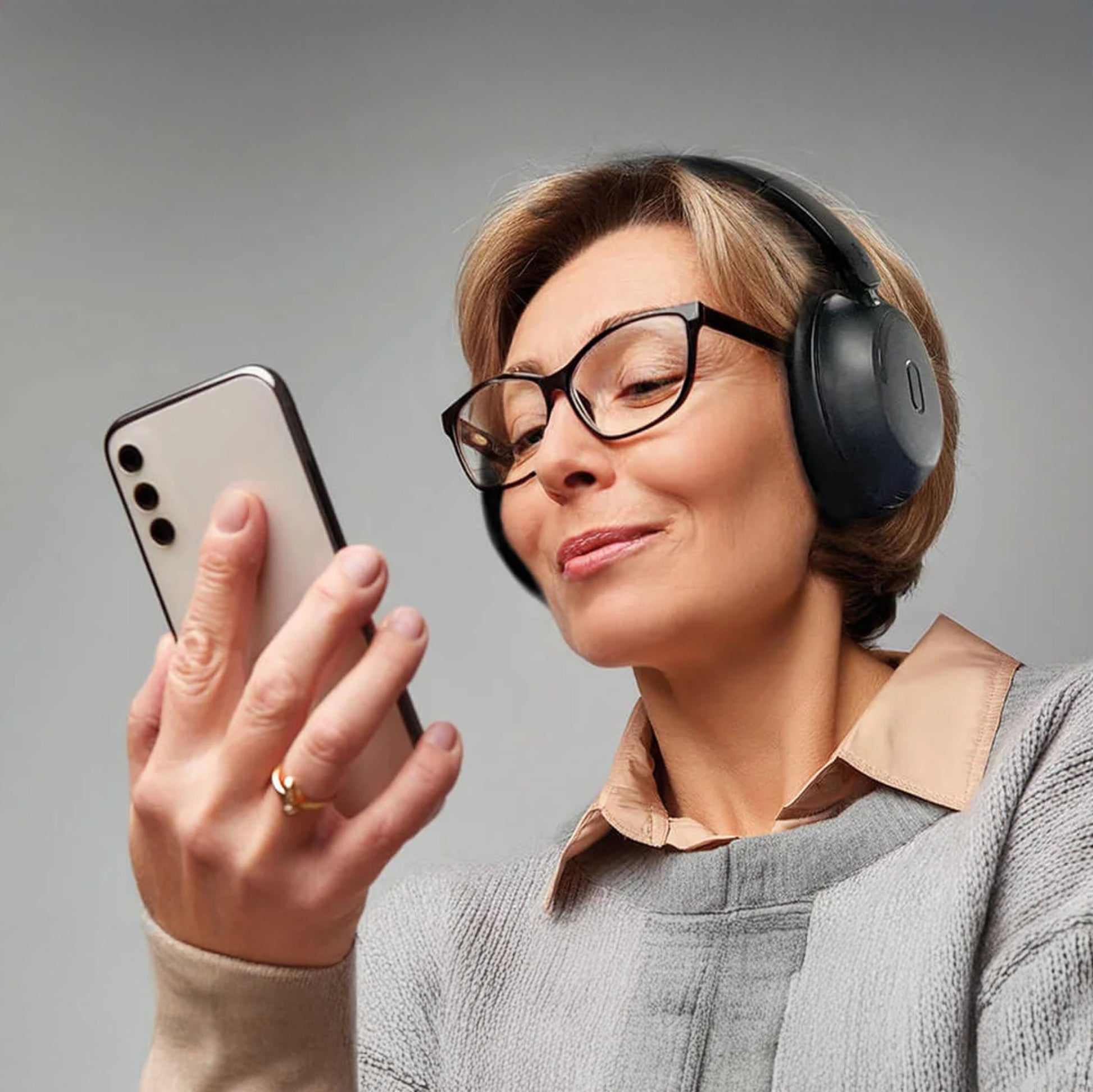 MIXX StreamQ Surround TV trådløse hovedtelefoner bæres af kvinde med briller, gråtøj og smartphone.