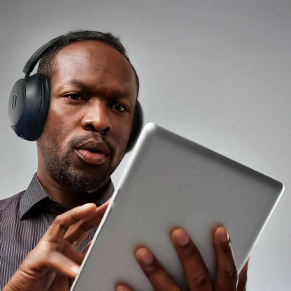 MIXX StreamQ Surround TV trådløse hovedtelefoner bæres af mand iført mørk skjorte, rører ved tablet.