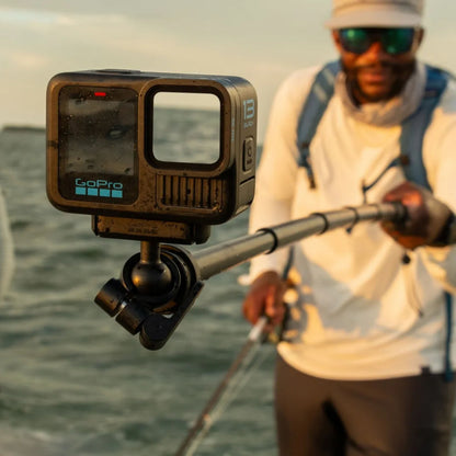 Gopro Magnetisk lås kugleled på forlængerstang, udendørs brug ved vand med person i fiskeudstyr i baggrunden.