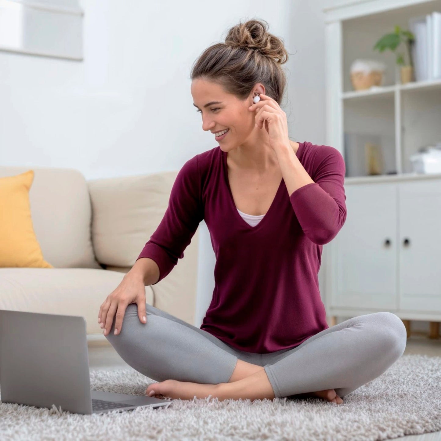 Hama Spirit Calm TWS øretelefoner sættes i øret af kvinde, laptop åben ved siden af, sofa og reol ses bagved.