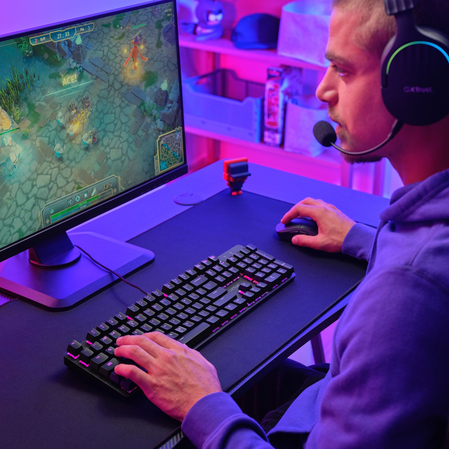 Trust GXT 871 Zora Mekanisk Gamingtastatur med Huano-switches og RGB-belysning i lilla og pink lys på skrivebord.