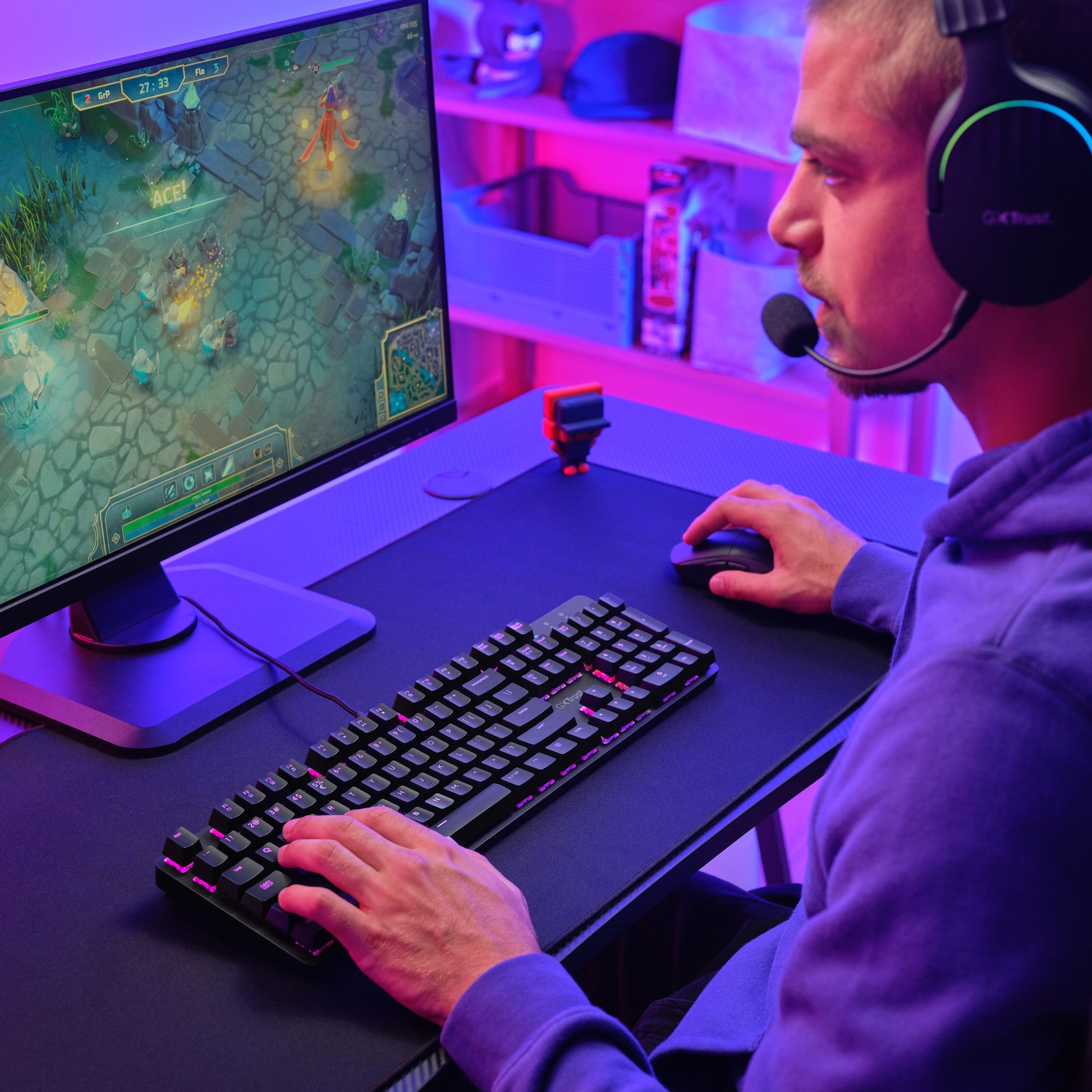 Trust GXT 871 Zora Mekanisk Gamingtastatur med Huano-switches og RGB-belysning i lilla og pink lys på skrivebord.