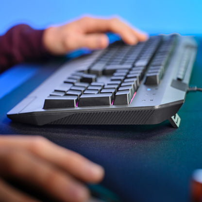 Trust GXT 836 Evocx RGB gamingtastatur og mus, tæt på hænder, farverigt RGB-lys reflekteres på skrivebord.