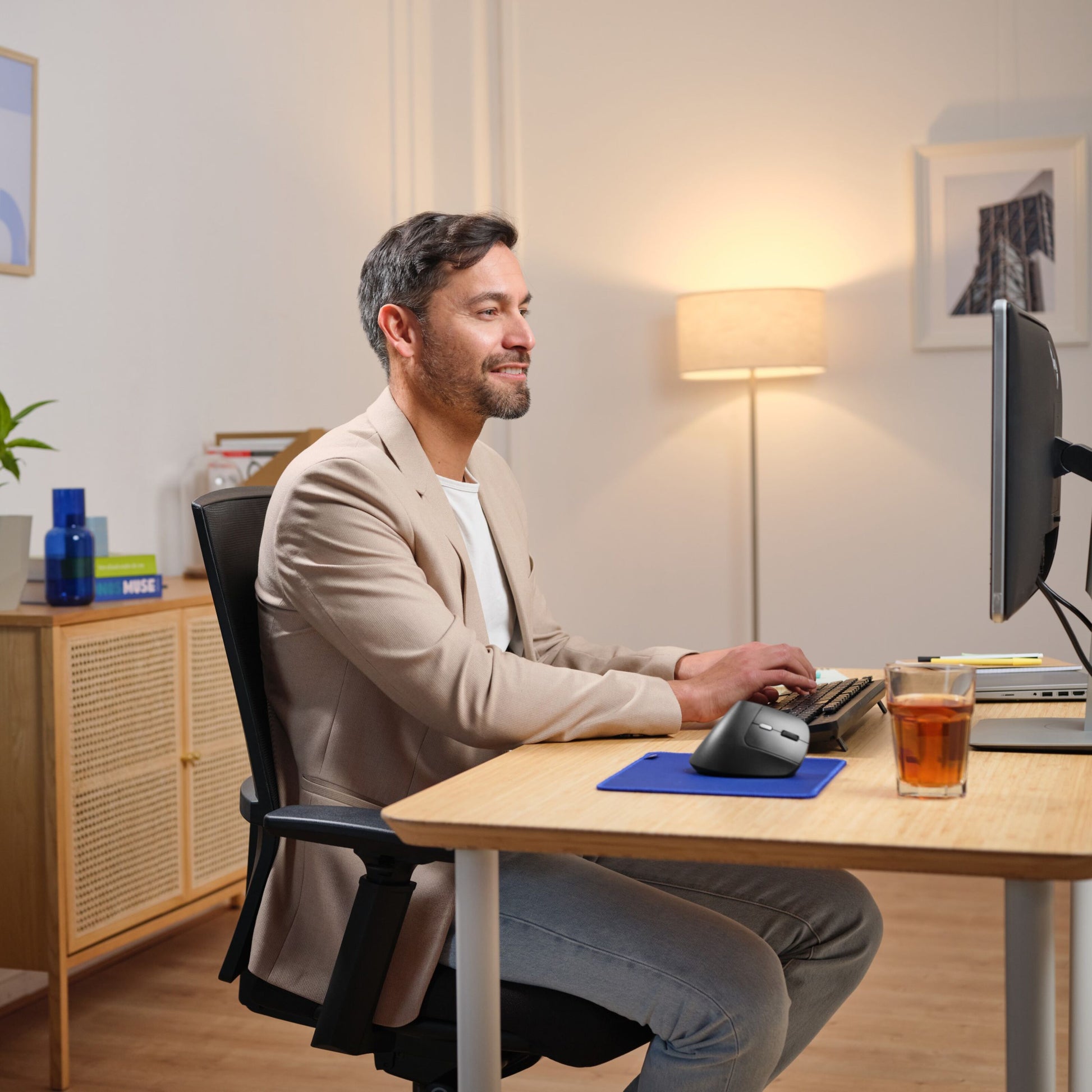 Trust Bayo II ergonomisk trådløs mus i brug ved skrivebord med tastatur og ekstra mus, mørk finish.