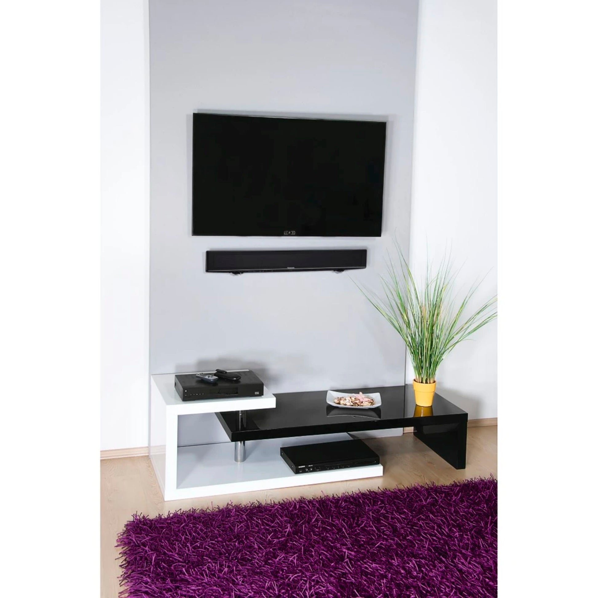 Fladskærms-tv monteret med Fleksibelt vægbeslag til soundbar, sort/hvid tv-møbel, gul potteplante, lilla tæppe.