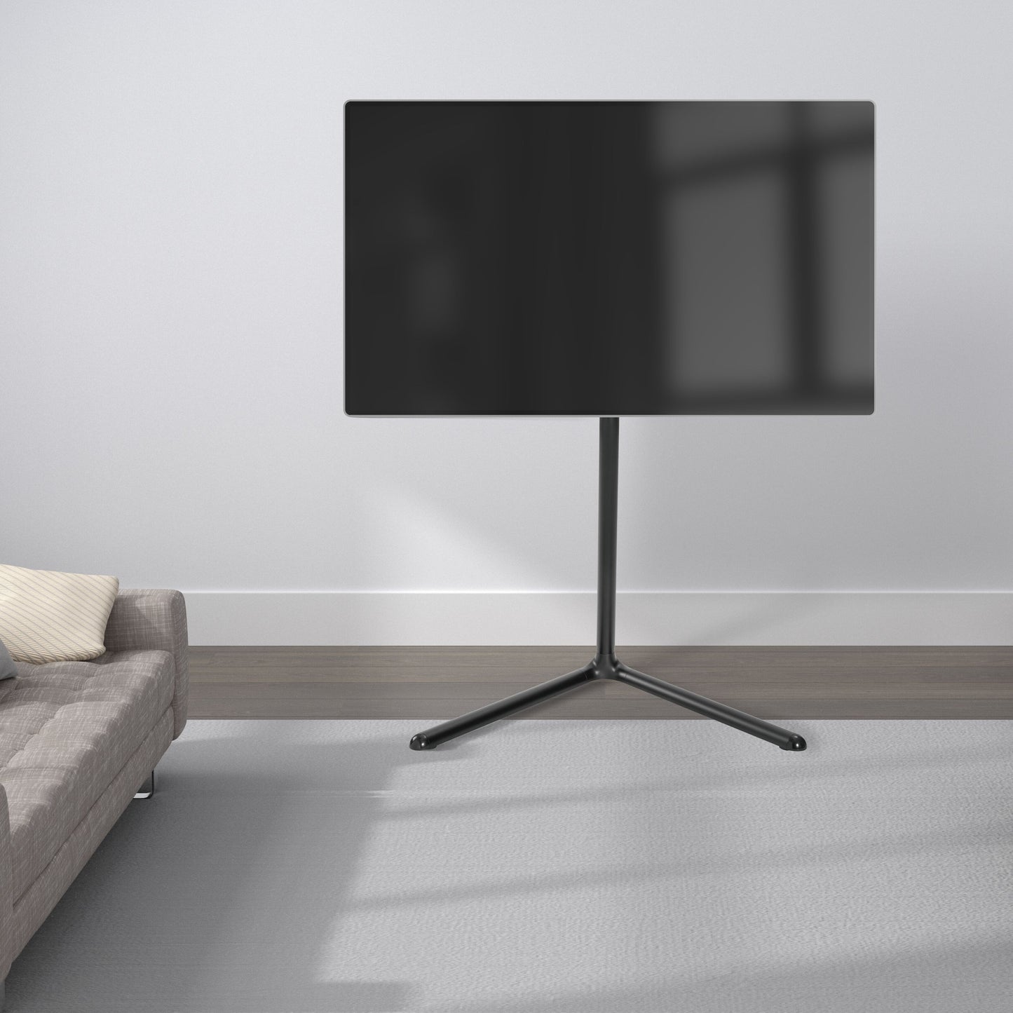 Nikabe V-base gulvstativ sort til tv 49-70 tommer med sort tv, grå sofa og mønstrede puder ses ved siden af.