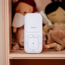 Alecto DBX130 Full Eco DECT-babyalarm hvid med lyd- og tovejskommunikation, sløret dukker i baggrunden.