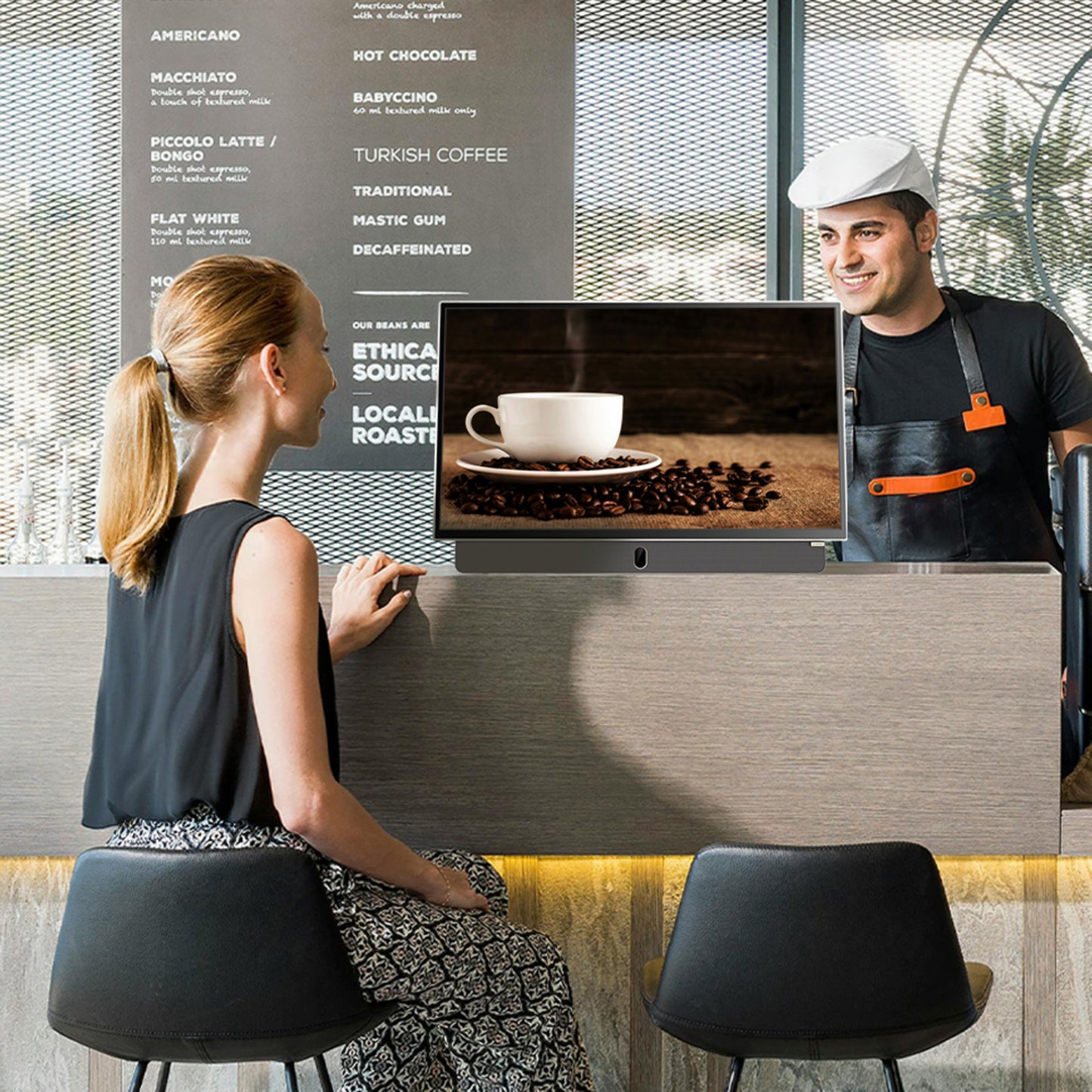Strong METZ 24" LED bærbar TV med Google TV vises på cafédisk ved siden af kaffekop og kaffebønner, menu i baggrunden.