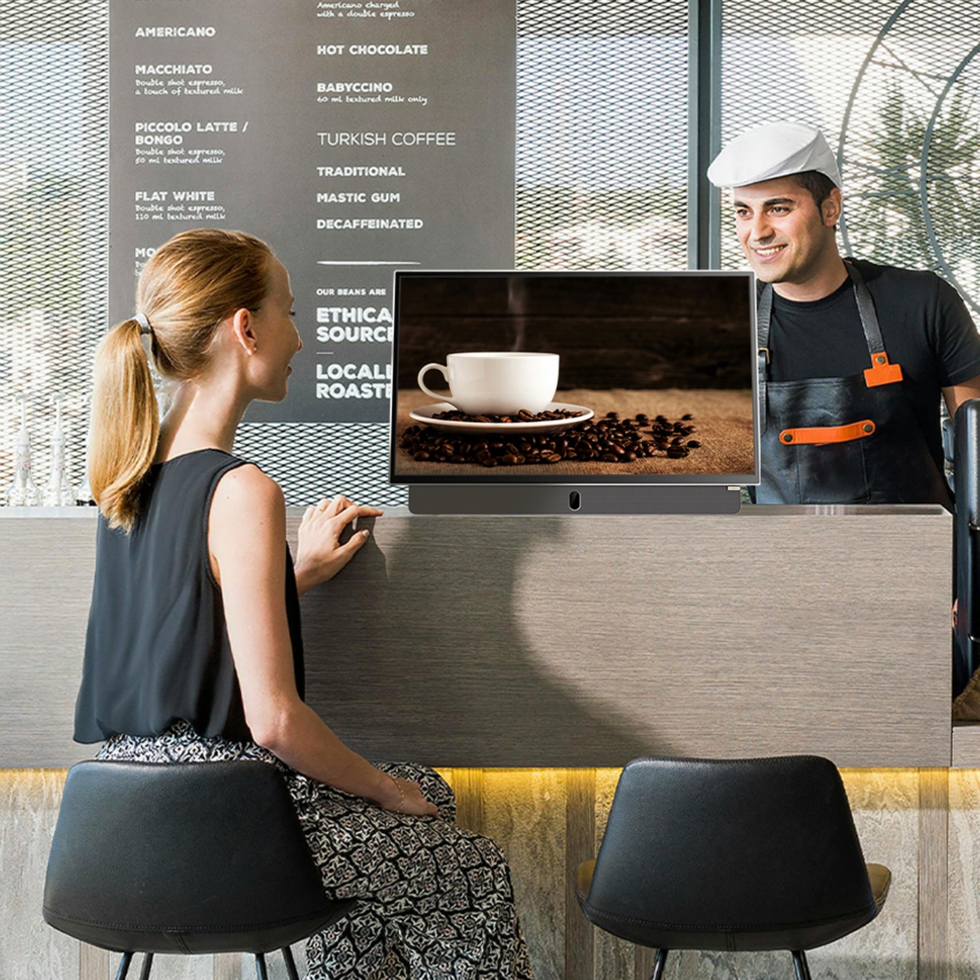 Strong METZ 24" LED bærbar TV med Google TV vises på cafédisk ved siden af kaffekop og kaffebønner, menu i baggrunden.