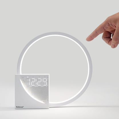 Rubicson Wake-up light vækkeur med natlampe, rundt LED ur, synlig hånd peger på display, model i lys grå nuance.
