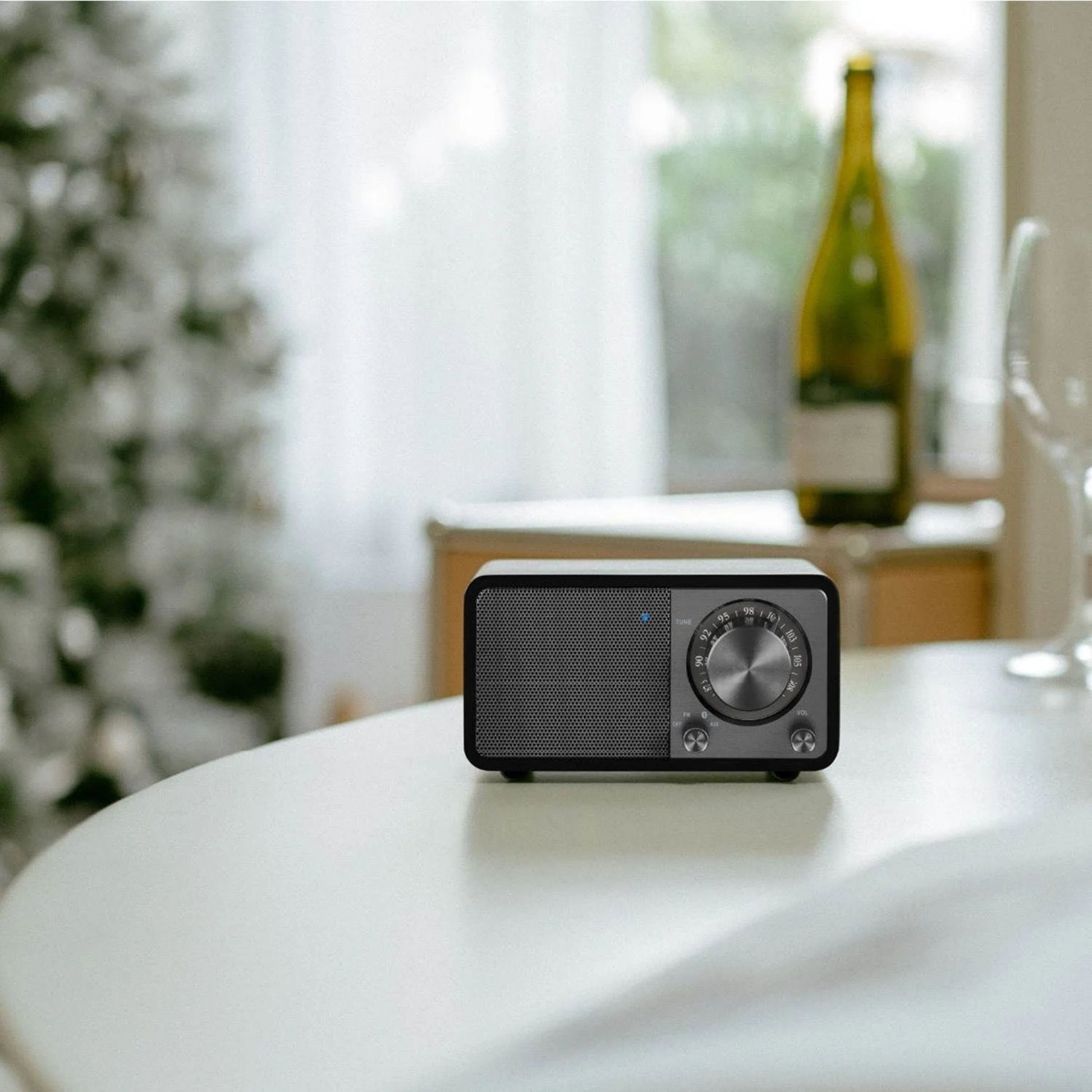 Sangean WR-7 PLUS FM-radio Midnight Oak streamer Bluetooth, står på bord med vinflaske og juletræ i baggrunden.