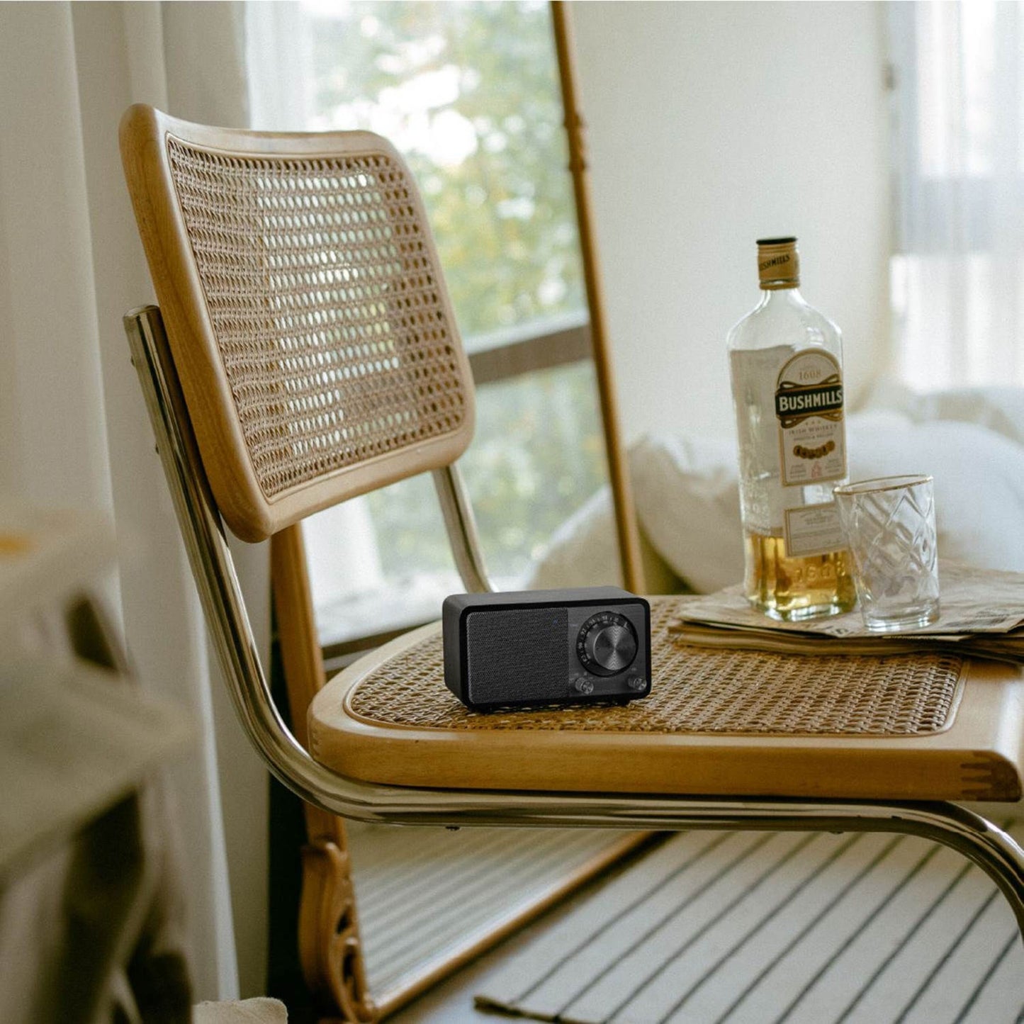 Sangean WR-7 PLUS Midnight Oak FM-radio på fletstol ved bord med Bushmills whiskeyflaske og glas med is.