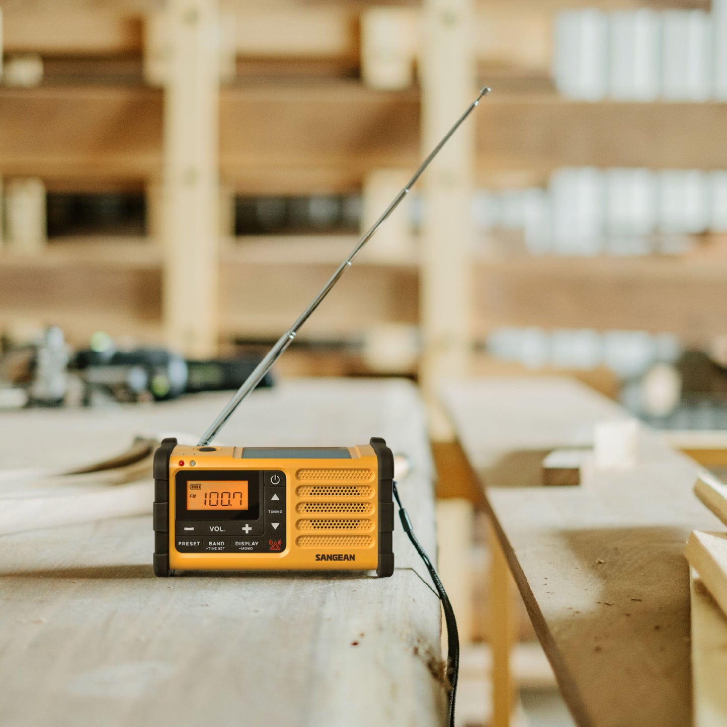 Sangean gul håndsvingradio til FM-signal med USB-C, antenne slået op, sat på træbord i værksted.
