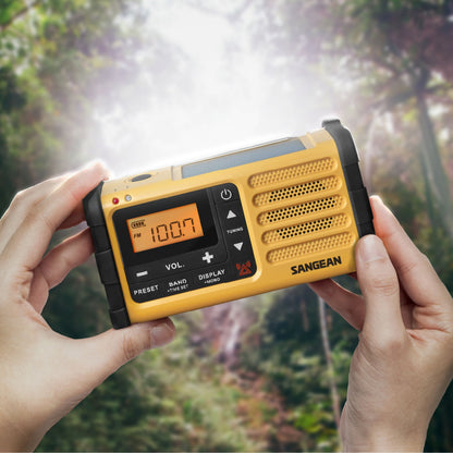 Sangean håndsvingradio FM gul, USB-C, orange digitalt display 100,7 MHz, nærbillede af hænder der holder radio.