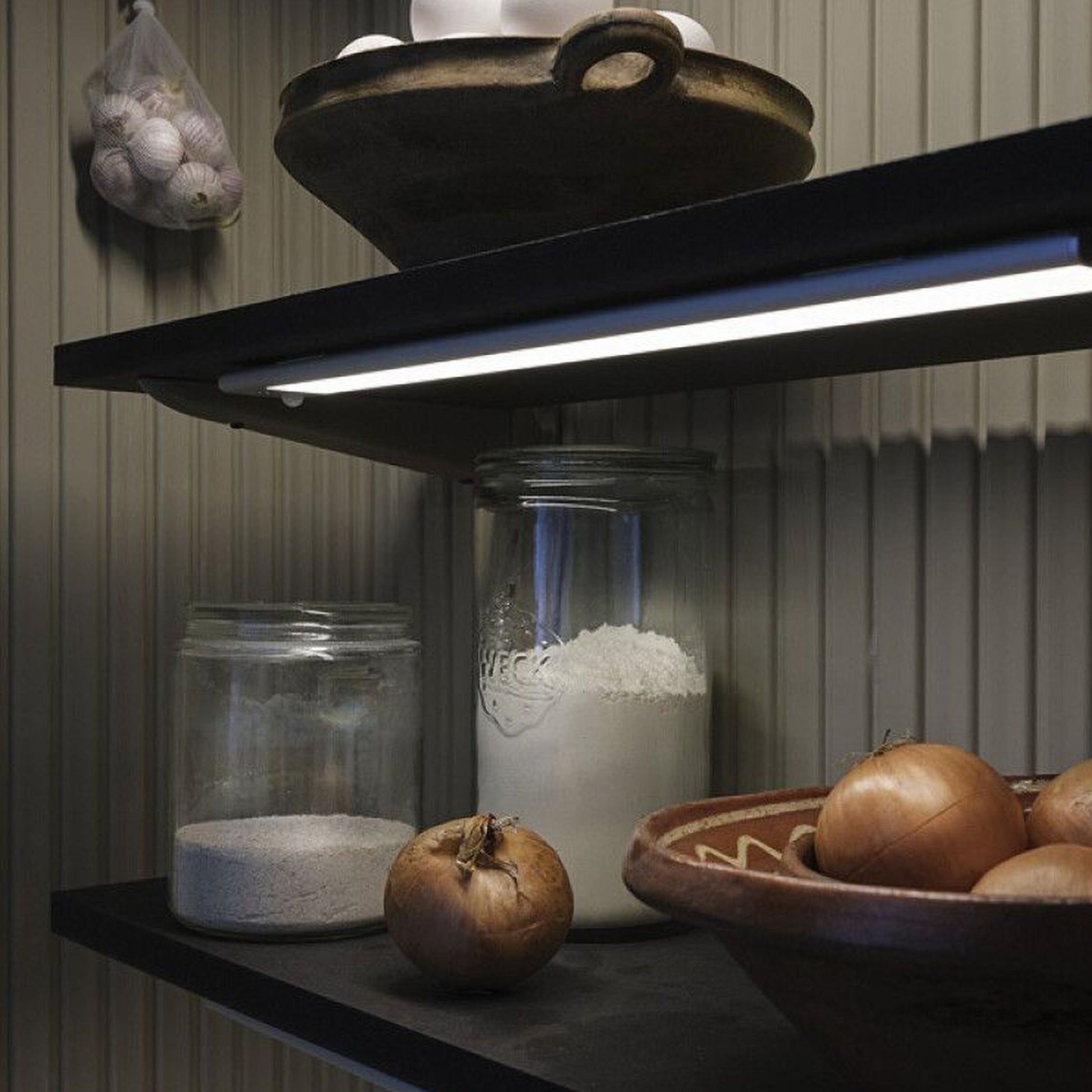 Glasbeholdere med mel og sukker på sort hylde oplyst af Lineær LED Underskabsbelysning med sensor 40cm, løg, æg, hvidløg.