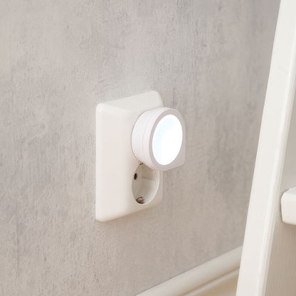 Luxorparts LED natlampe Mini i hvid stikkontakt på lysegrå væg ved siden af hvidt møbel, lyser med blødt hvidt skær.