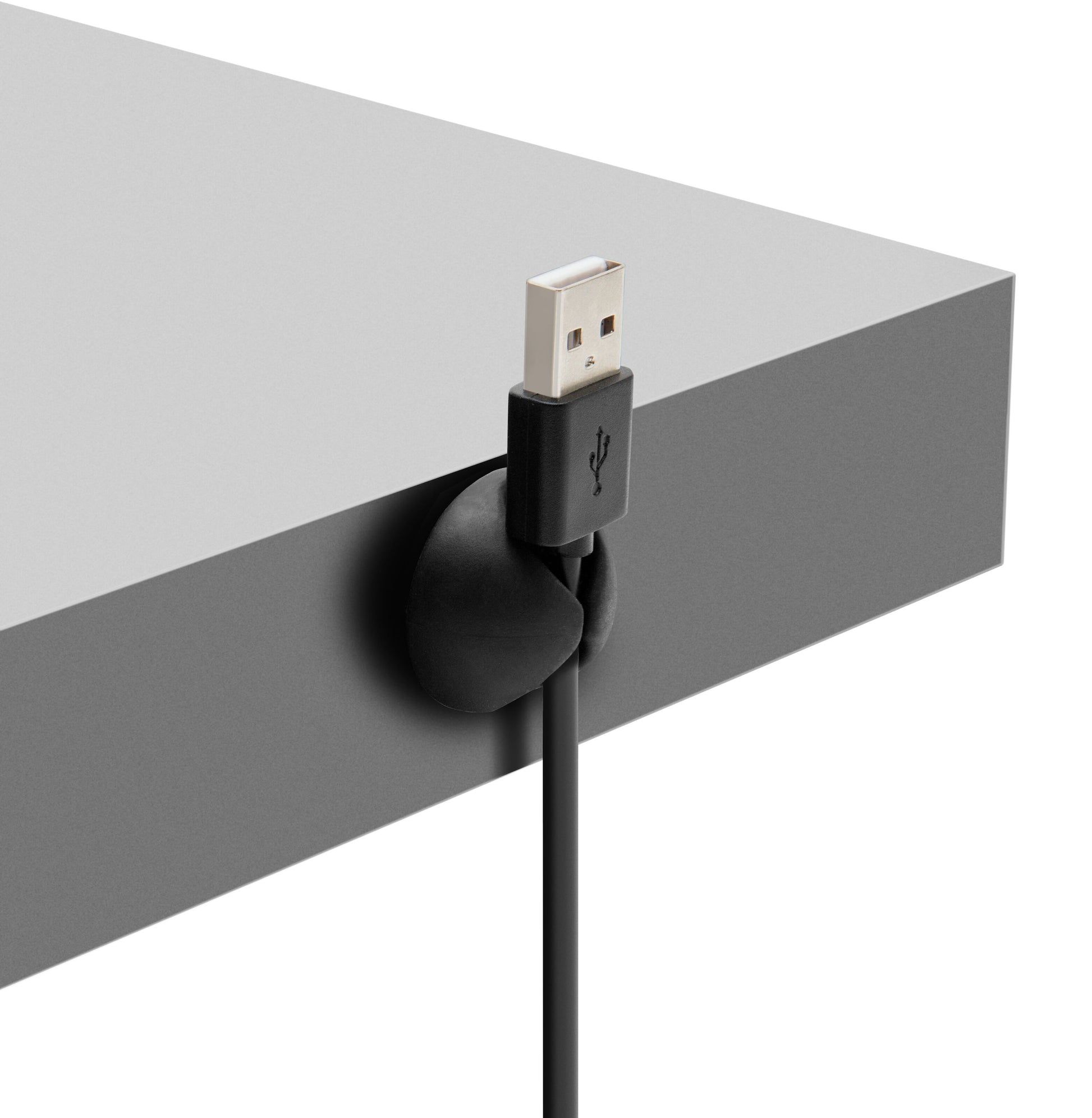 Sort USB-kabel fastgjort til grå bordkant med rund Luxorparts Selvklæbende kabelholder til computer- og mobilkabler.