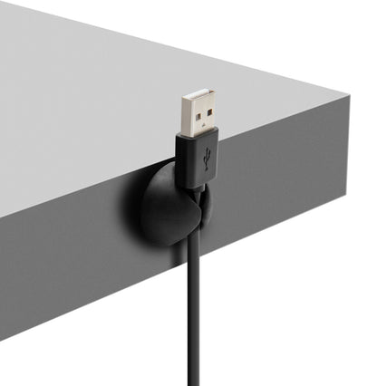Sort USB-kabel fastgjort til grå bordkant med rund Luxorparts Selvklæbende kabelholder til computer- og mobilkabler.