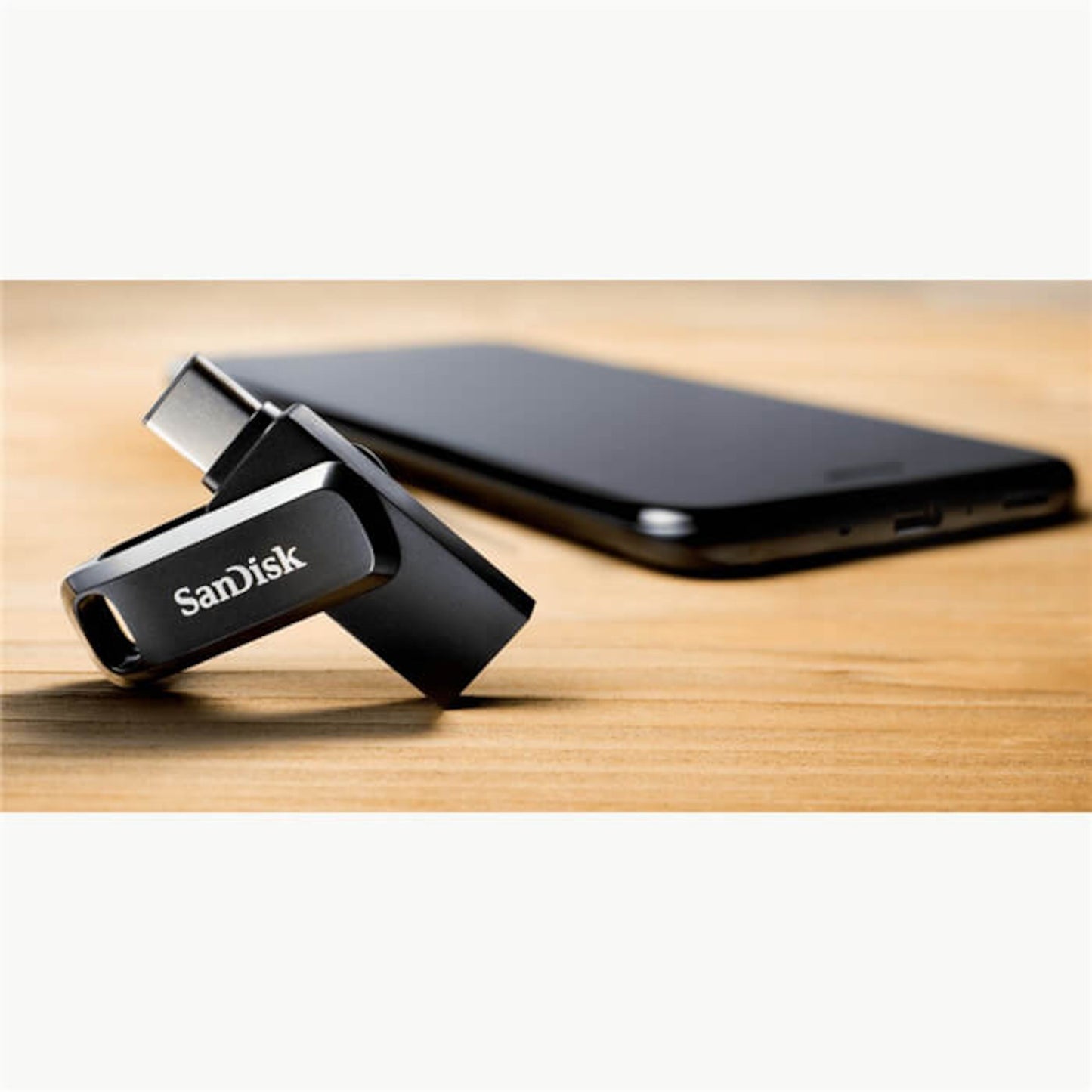 Sandisk Ultra Dual Drive Go USB-nøgle USB-C 128 GB, drejelig design, placeret ved siden af sort smartphone på træoverflade.