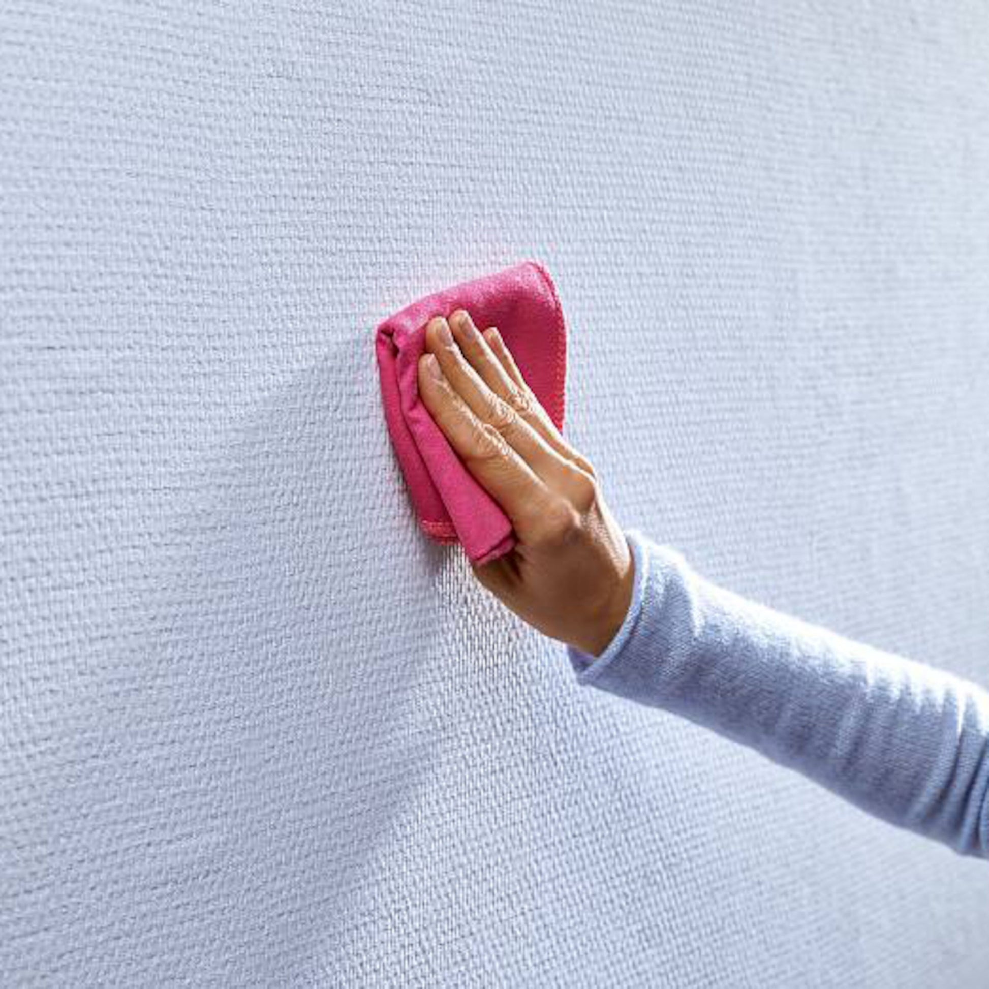 Tesa Ståltråd til tapet og gips 1 kg 2-pakning, hånd i lyseblå ærme tørrer hvid væg med pink klud.