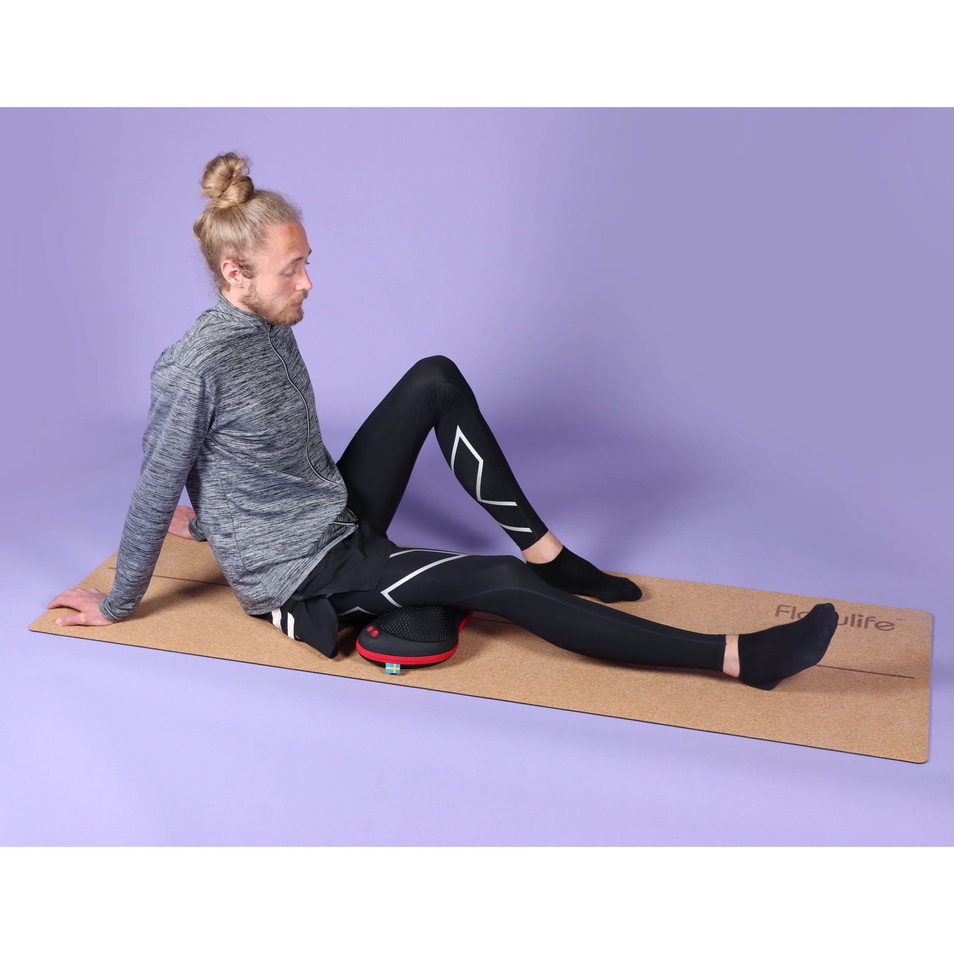Flowpillow Varmemassagepude fra Flowlife brugt på yogamåtte, person iført grå langærmet trøje og sorte leggings.