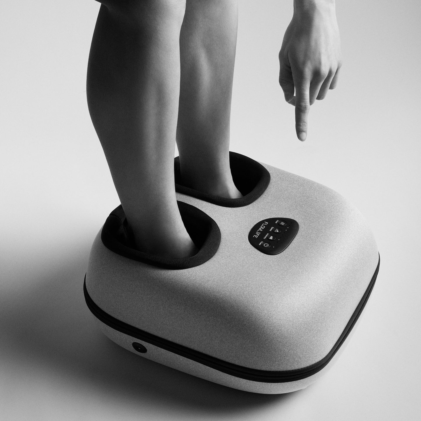 Flowlife Flowfeet Heat fodmassage, begge fødder i enheden, finger peger mod digitalt kontrolpanel, sort-hvid.