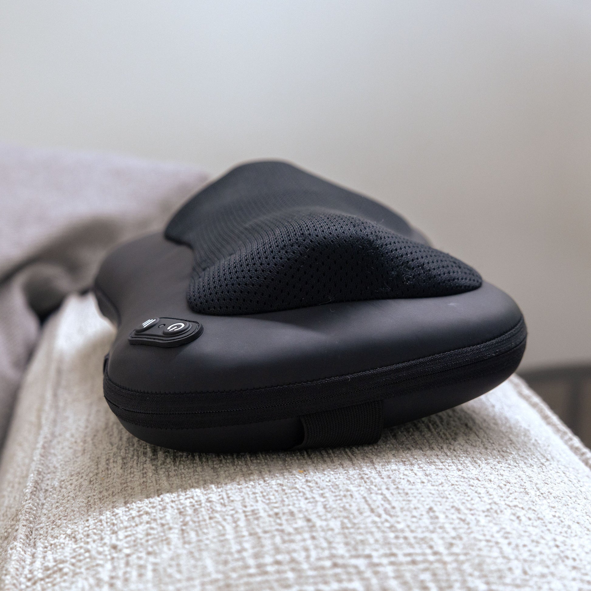 Shiatsu massagepude med varme, mesh-betræk, kontrolknapper og genopladelig funktion på lyst stof ved beige tæppe.