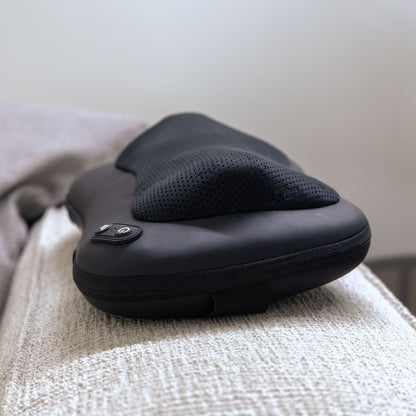 Shiatsu massagepude med varme, mesh-betræk, kontrolknapper og genopladelig funktion på lyst stof ved beige tæppe.