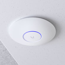 Ubiquiti UniFi U6+ WiFi 6 access point, rund, hvid, blå LED-ring, Ubiquiti-logo, monteret i hvidt loft, PoE 802.11af.