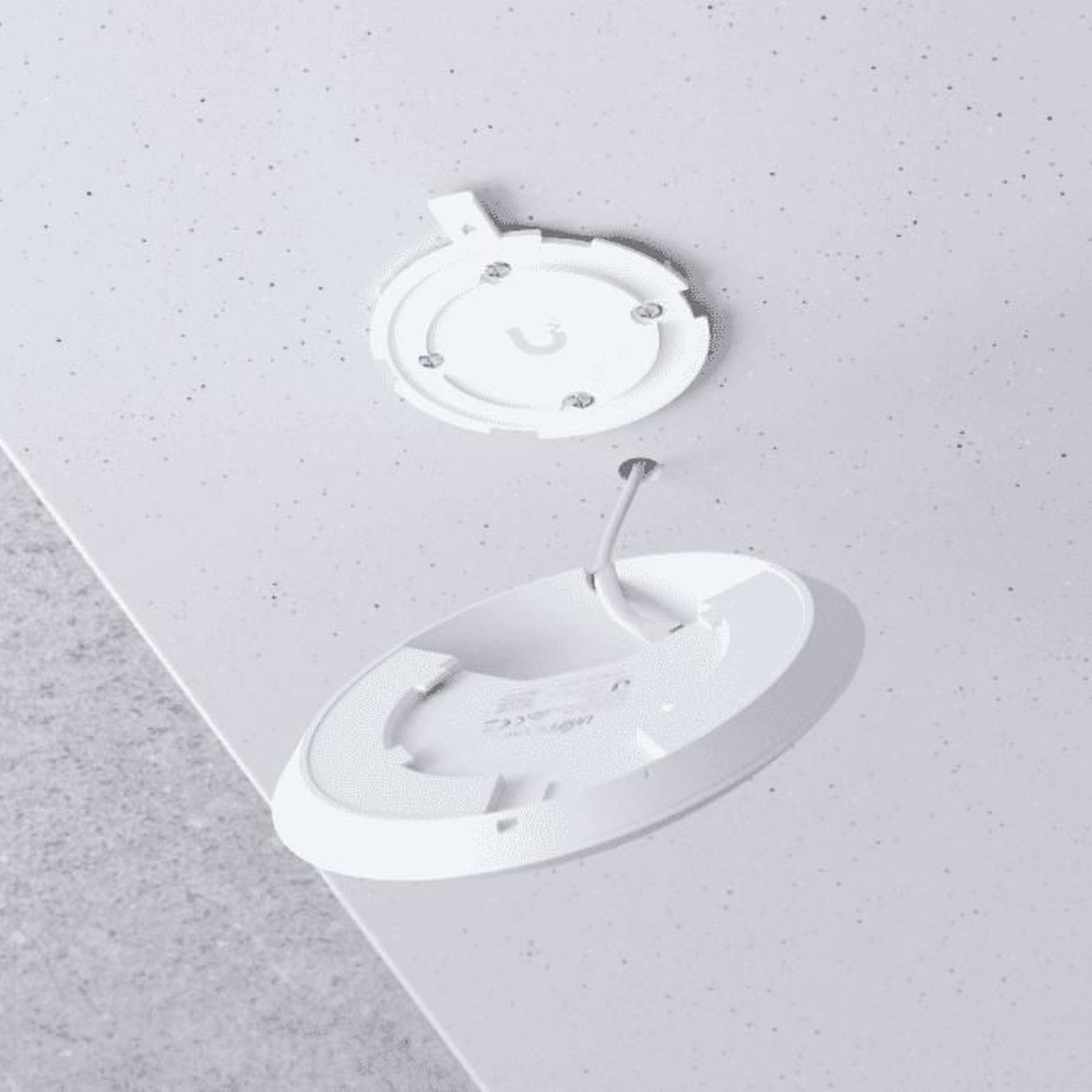 Hvid trådløs opladningspad indbygget i lys bordplade, åben låg viser kabel, ved siden af UniFi U6+ WiFi 6 access point.