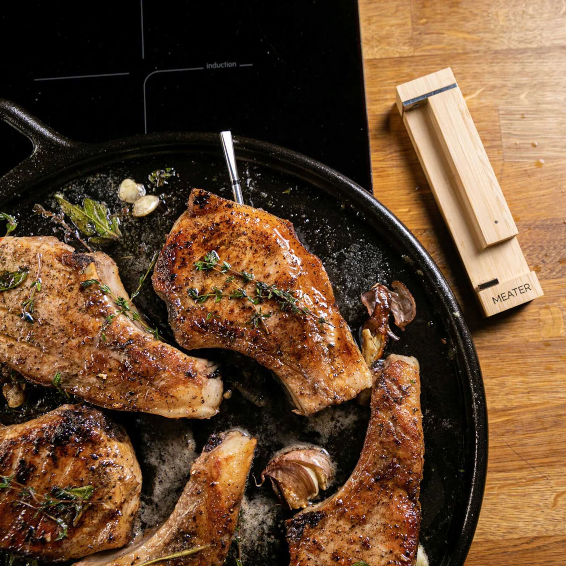Meater 2 Plus trådløs grilltermometer med repeater i svinekotelet, træetui synligt ved siden af på køkkenbord.